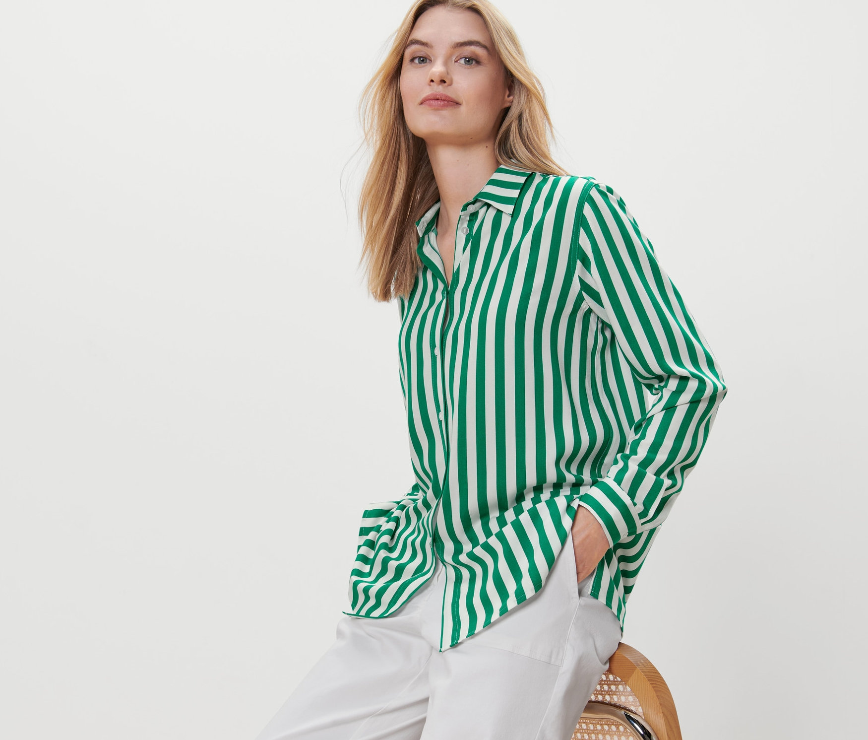 Sarışın bir kadın sandalyede oturuyor ve yeşil çizgili bir bluz giyiyor.