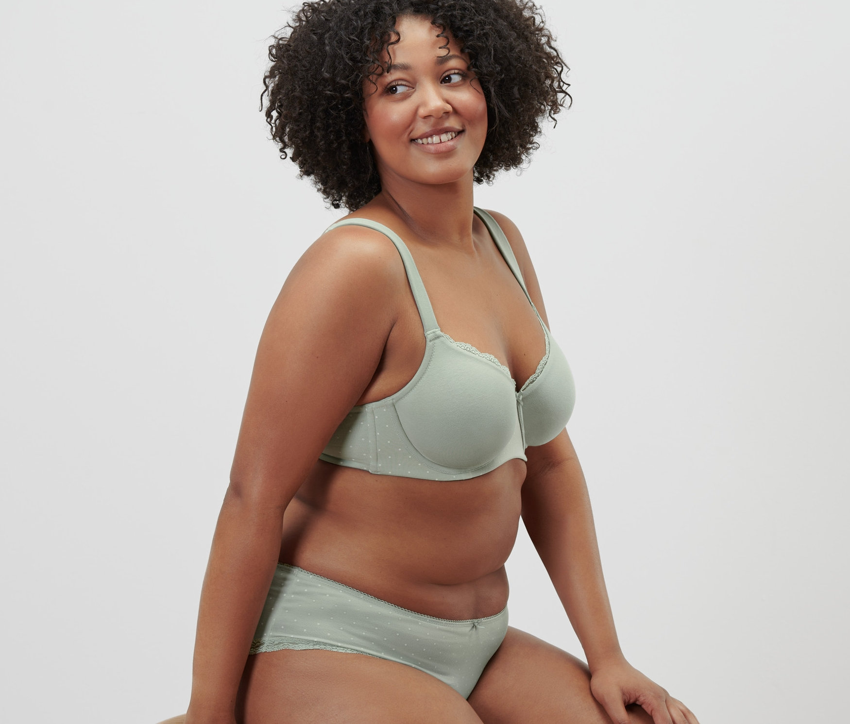 Kadın taburede oturuyor, ada çayı yeşili balenli sütyen giyiyor.