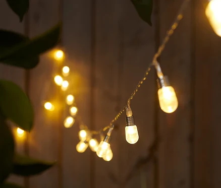 Mini ampullü LED ışık zinciri ahşap bir çitin önünde asılı duruyor.