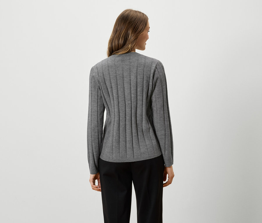 Kadın arkadan gri, uzun kollu bir üst ve siyah pantolon giyiyor.