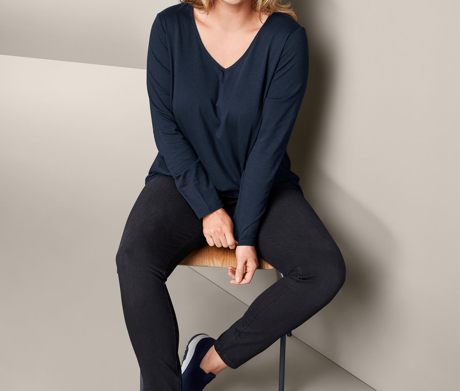 Kadın sandalyede oturuyor, siyah kot pantolon ve lacivert Uzun Kollu Tişört giyiyor.