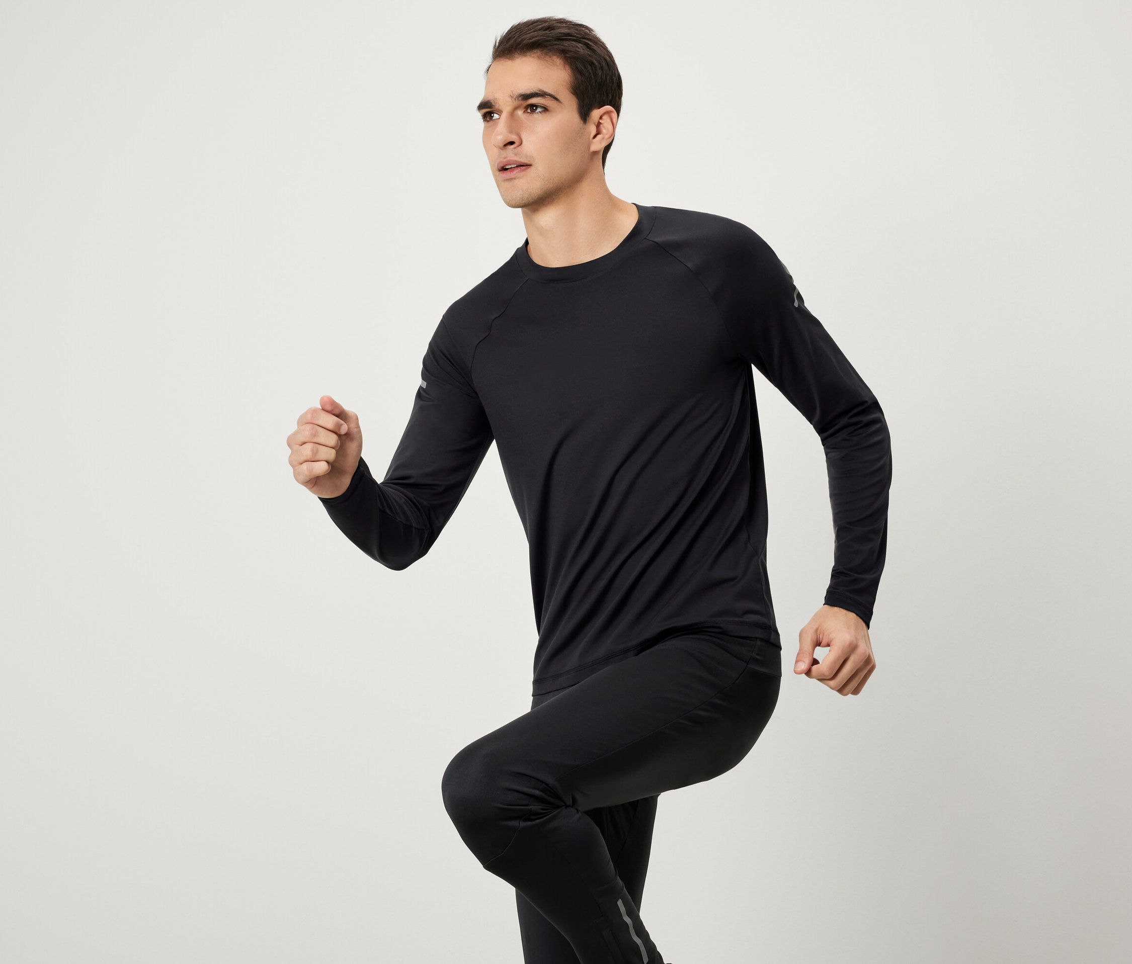 Siyah uzun kollu spor giyim ve pantolonlu bir adam koşuyor.