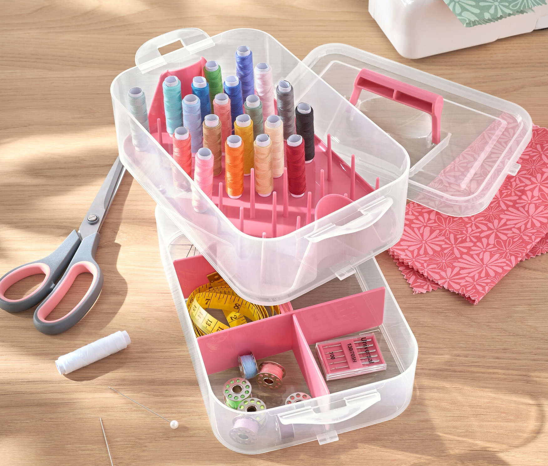 Açık plastik alet kutusu, iplikler, makas, iğneler ve dikiş makinesi bir masa üzerinde duruyor.