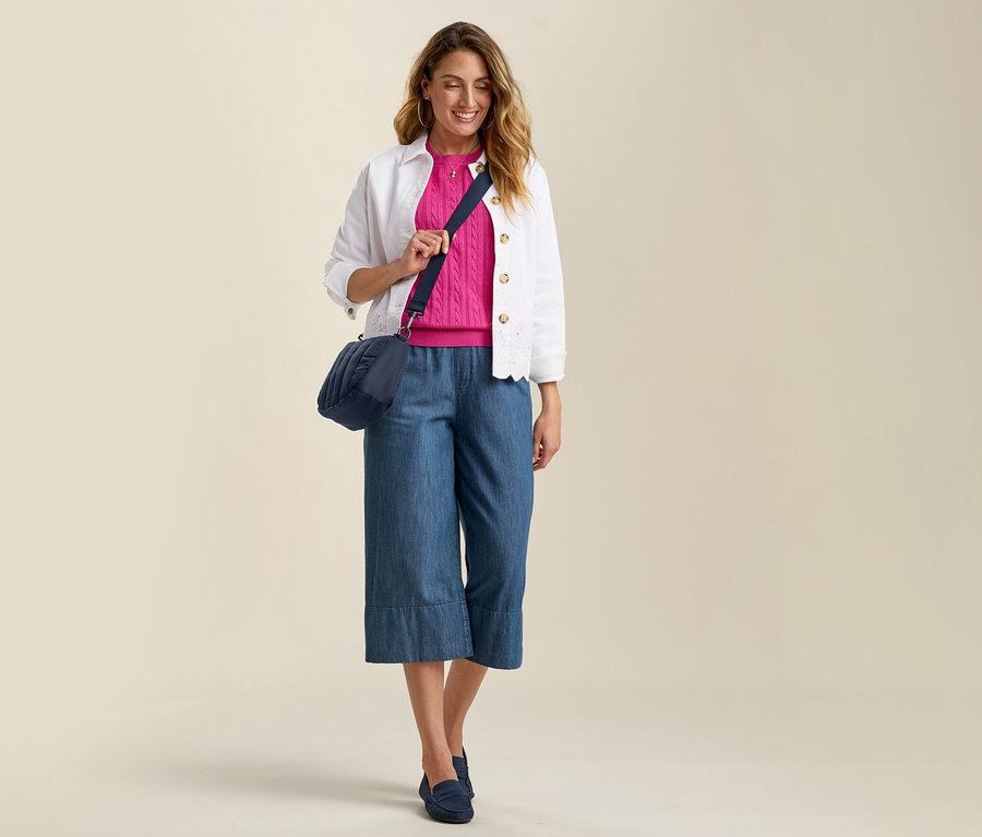Kot pantolon, pembe kazak ve ajurlu denim ceket giyen kadın. Mavi çapraz askılı çanta ve uyumlu loafer'lar.