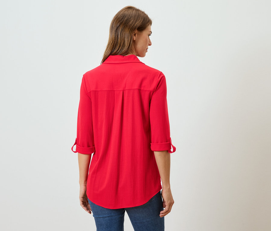 Uzun kahverengi saçlı, kırmızı uzun kollu bluz ve kot pantolon giyen bir kadının arka görünümü.