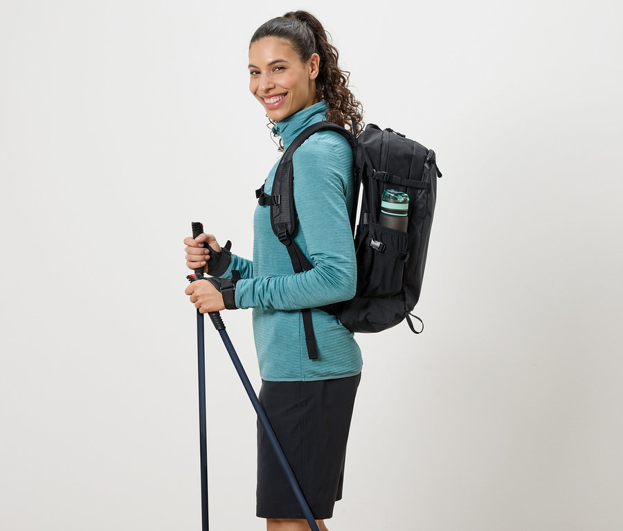 Turkuaz balıkçı yaka kazaklı, sırtında siyah sırt çantası olan ve yürüyüş batonları tutan kadın.