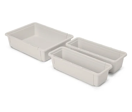 Beyaz bir arka plan üzerinde duran üç boş, bej renkli plastik çekmece düzenleyici.