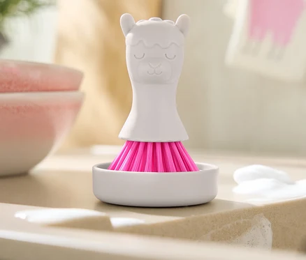 Pembe kıllı beyaz lama şeklindeki fırça, sabun kalıntılarının olduğu lavabonun üzerinde beyaz bir kapta duruyor.