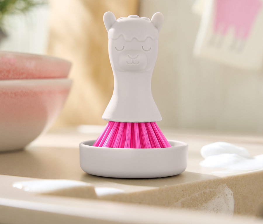 Pembe kıllı beyaz lama şeklindeki fırça, sabun kalıntılarının olduğu lavabonun üzerinde beyaz bir kapta duruyor.