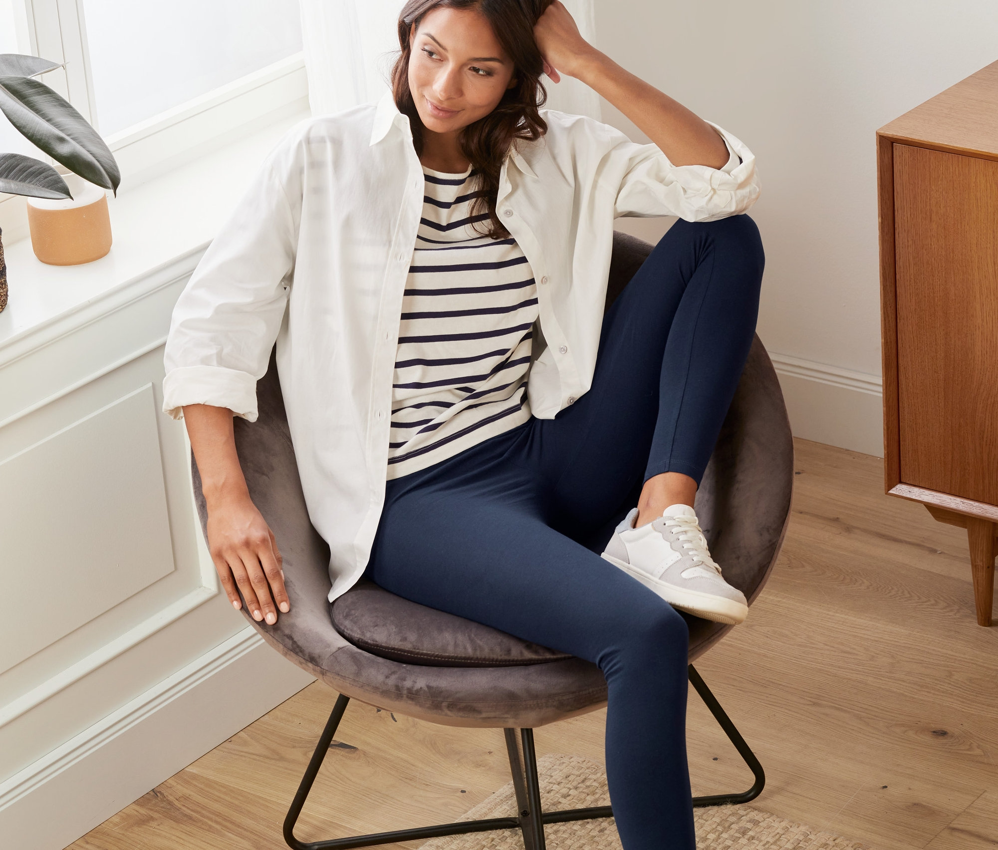 Kadın koltukta oturuyor ve lacivert tayt giyiyor.