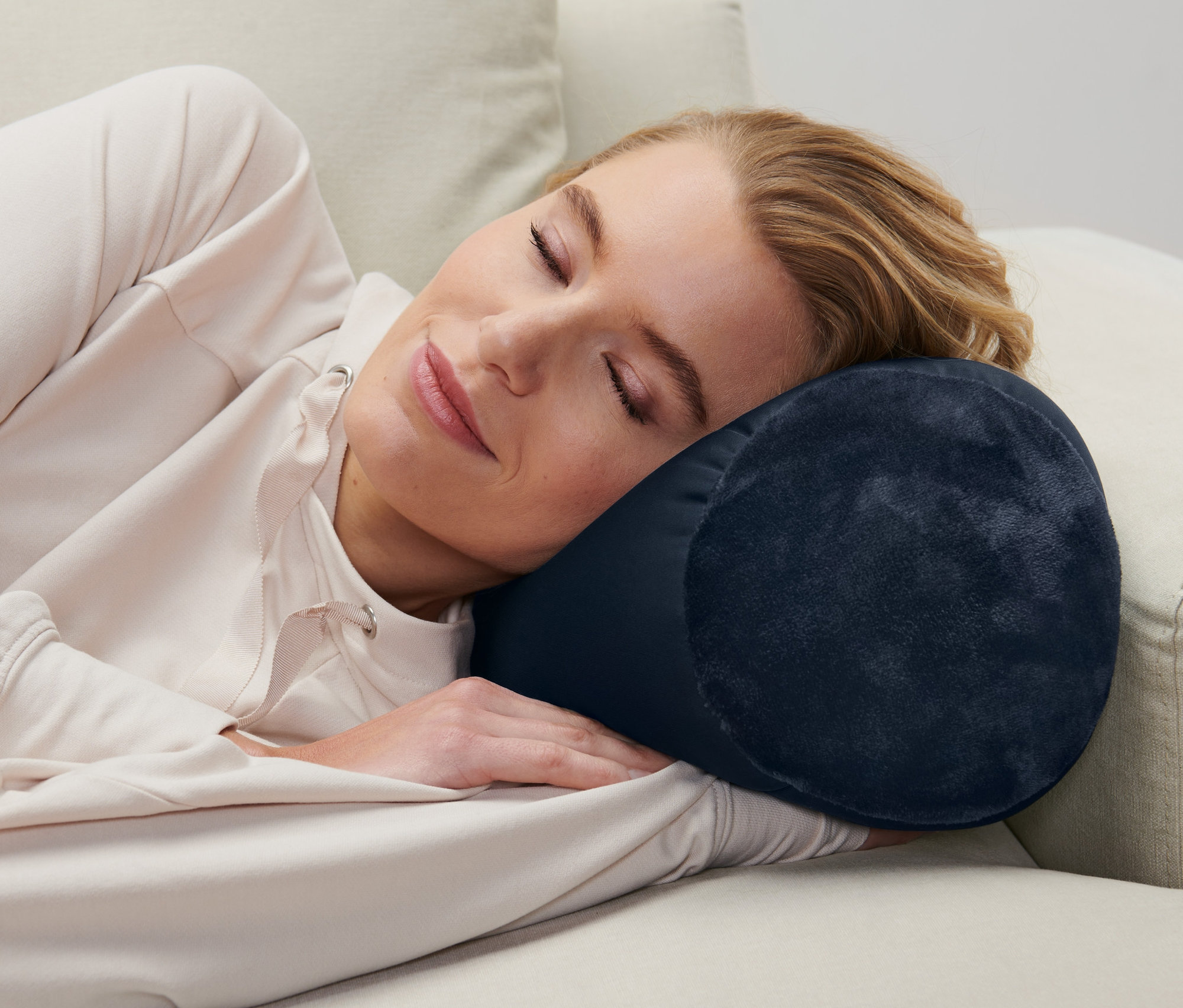 Kadın kanepede yatıyor ve mavi bir Rahatlama Yastığı kullanıyor.