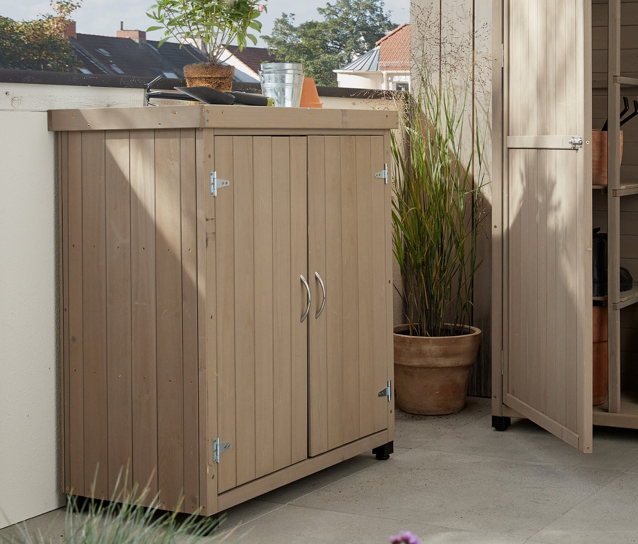 Bir terasta iki adet »Jonte« bahçe dolabı. Büyük dolabın kapısı açık ve açılır masası var.