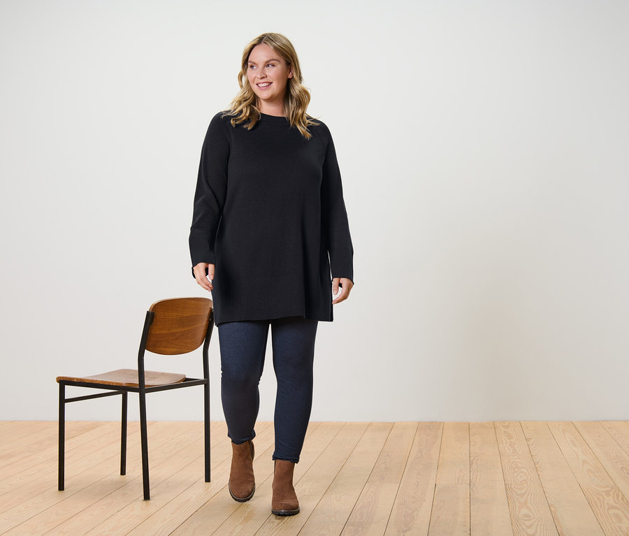 Bir kadın, uzun örgü, koyu kahve bir kazak ve içi astarlı kot görünümlü bir tayt giyerek yürüyor.