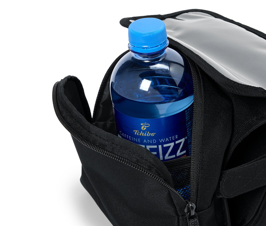 Açık siyah bir çantanın içinde mavi bir şişe Tchibo Caffeine and Water Fizz var.
