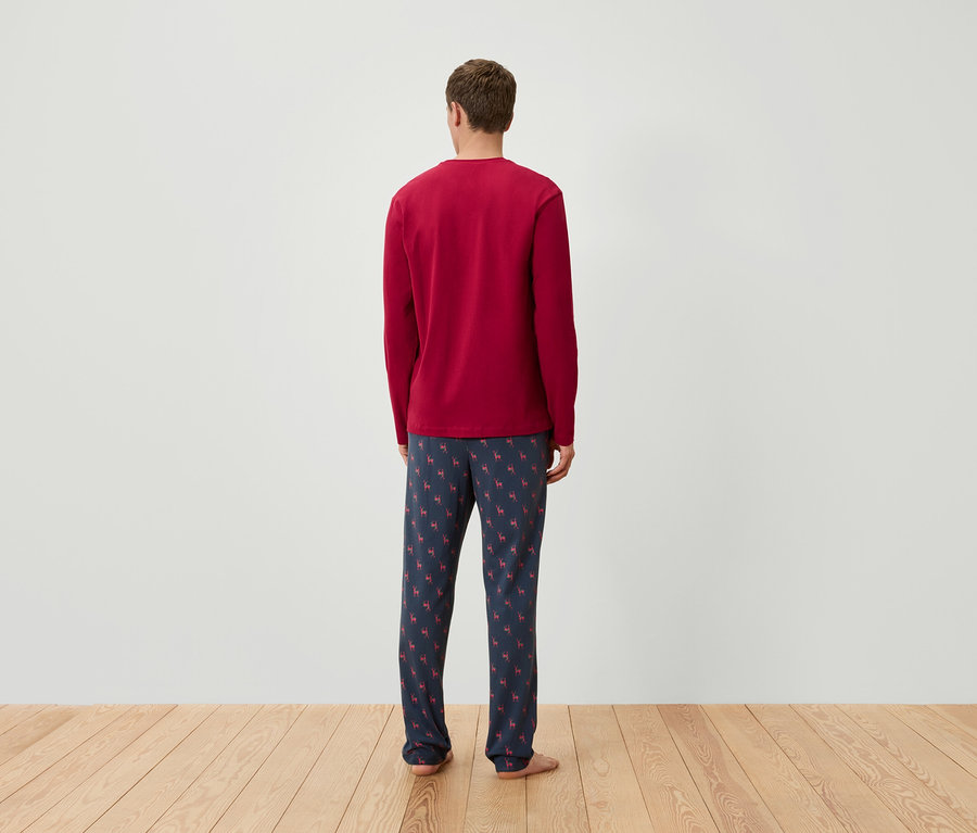 Arkası dönük bir adam, uzun kollu kırmızı bir pijama üstü ve ren geyiği desenli lacivert bir pijama altı giyiyor.