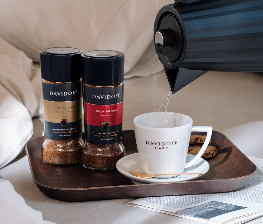Bir kişi su ısıtıcısından DAVIDOFF CAFÉ fincanına su döküyor. Yanında tepside DAVIDOFF CAFÉ Fine Aroma 100g Instantkaffee ve DAVIDOFF CAFÉ Fine Aroma 90g Instantkaffee duruyor.