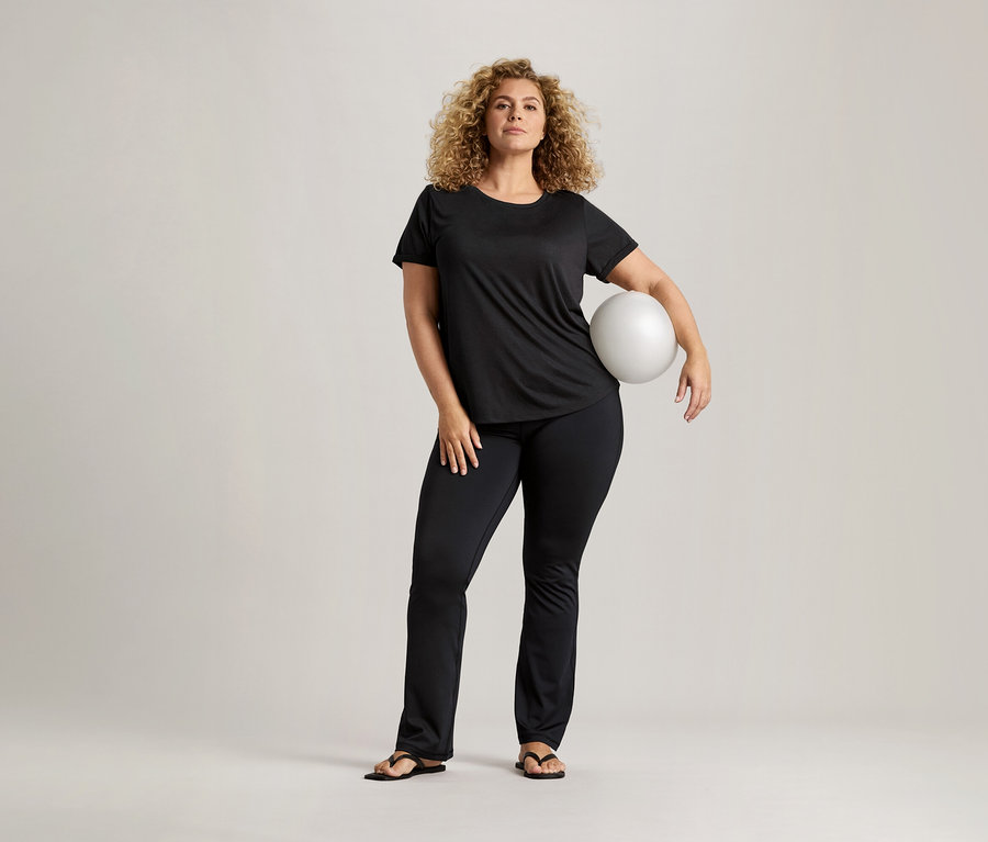 Kıvırcık saçlı, siyah tişörtlü ve siyah pantolonlu kadın beyaz bir top tutuyor.