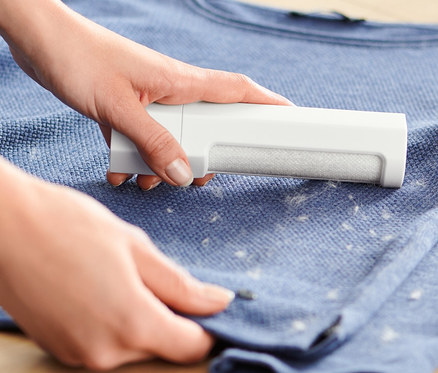 Kadın, mavi bir kazağın üzerinde elbise fırçası kullanıyor.