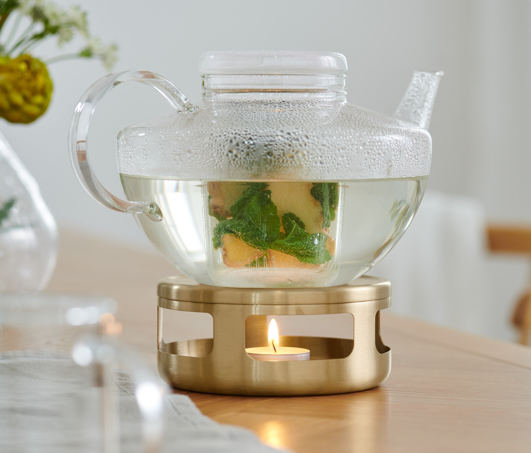 İçinde çay olan şeffaf cam demlik, altın renkli mumlu ısıtıcının üzerinde duruyor.
