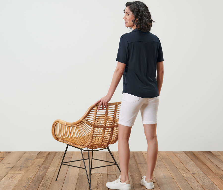 Kadın kameraya arkası dönük duruyor, üzerinde lacivert düğmeli bluz var.