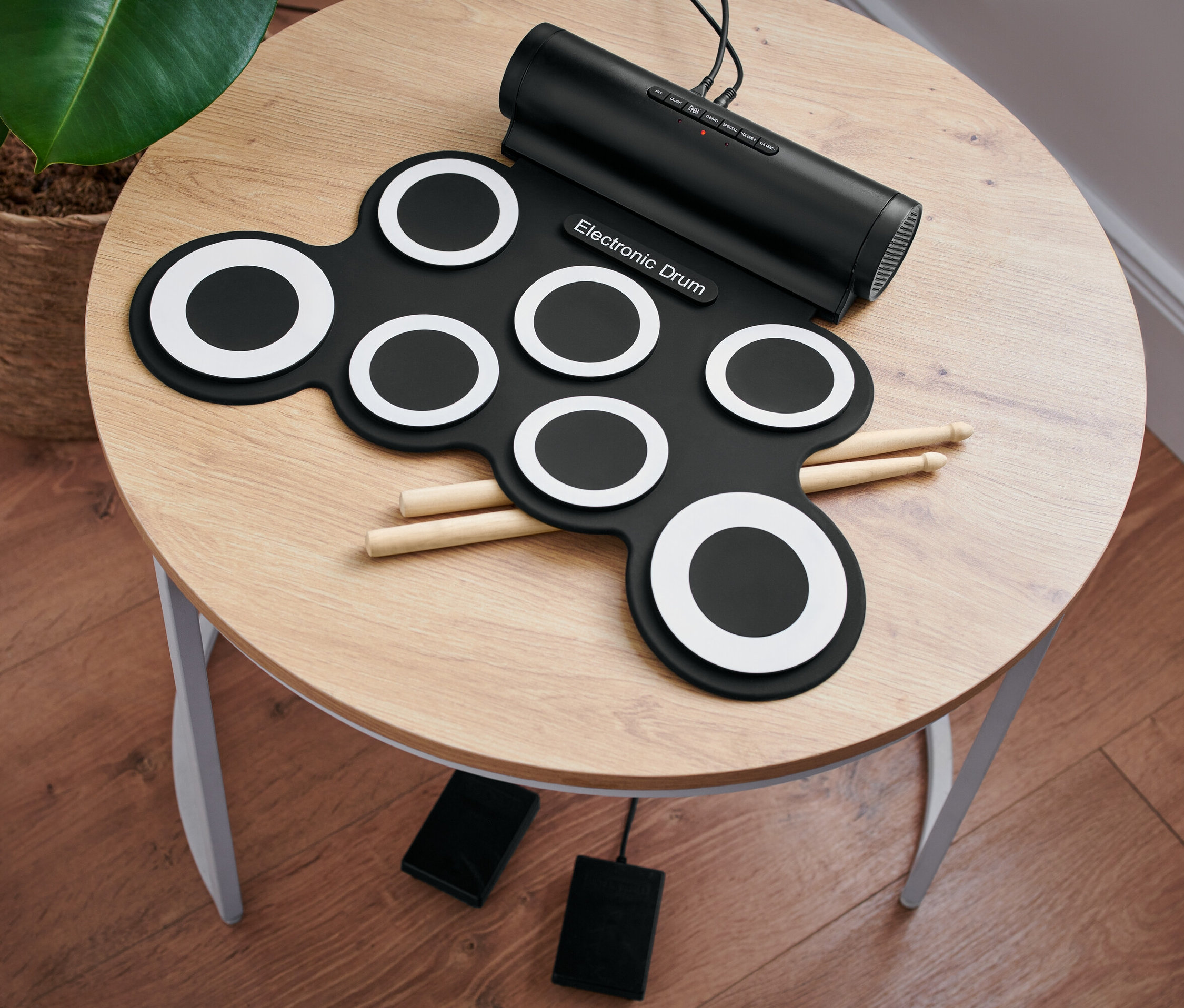 Yuvarlak bir masa üzerinde baget ve pedalları olan bir elektronik bateri seti duruyor.