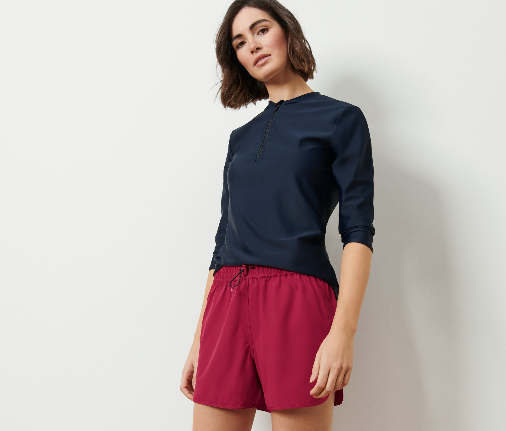 Kadın lacivert, üç çeyrek kollu bir üst ve mürdüm şort mayo ile poz veriyor.