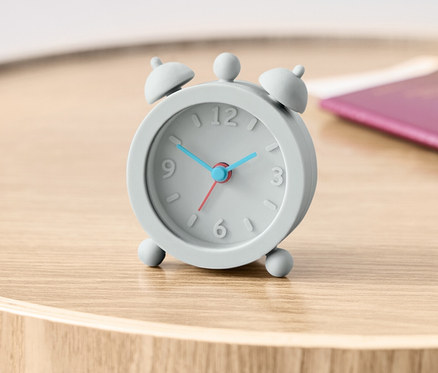 Ahşap bir masanın üzerinde pasaportun yanında gri bir Yolculuk Çalar Saati duruyor.