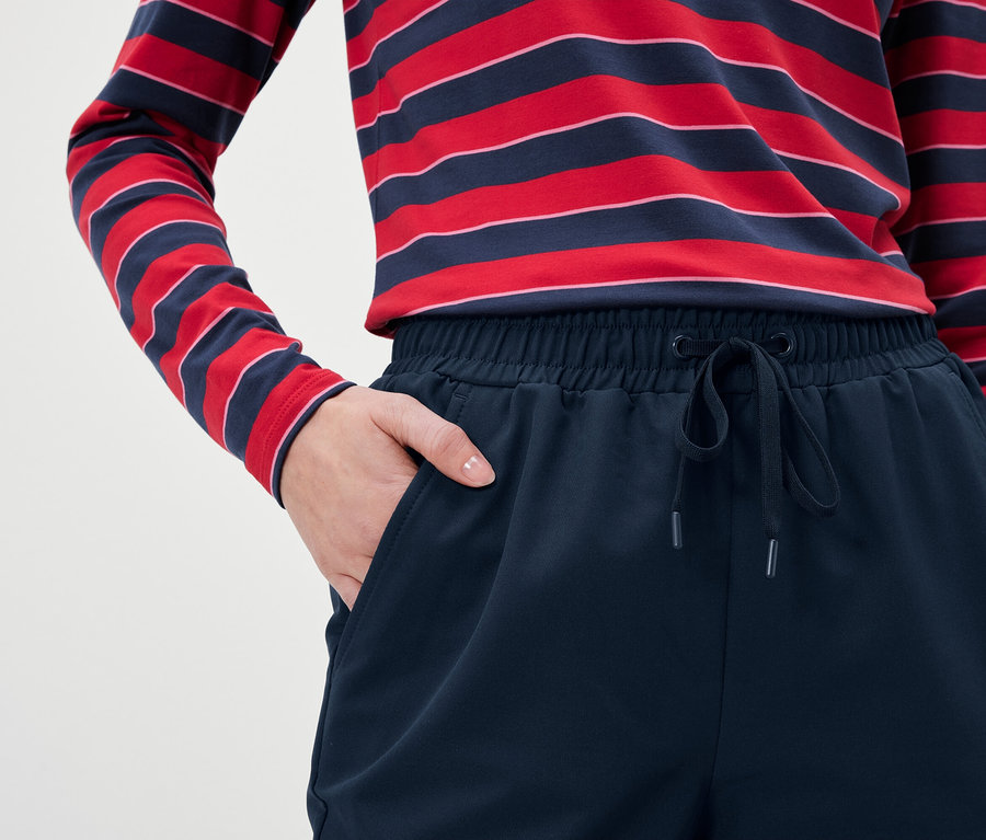 Lacivert eşofman altı ve kırmızı-mavi çizgili uzun kollu tişört giyen bir kadının, eli cebinde detayı.