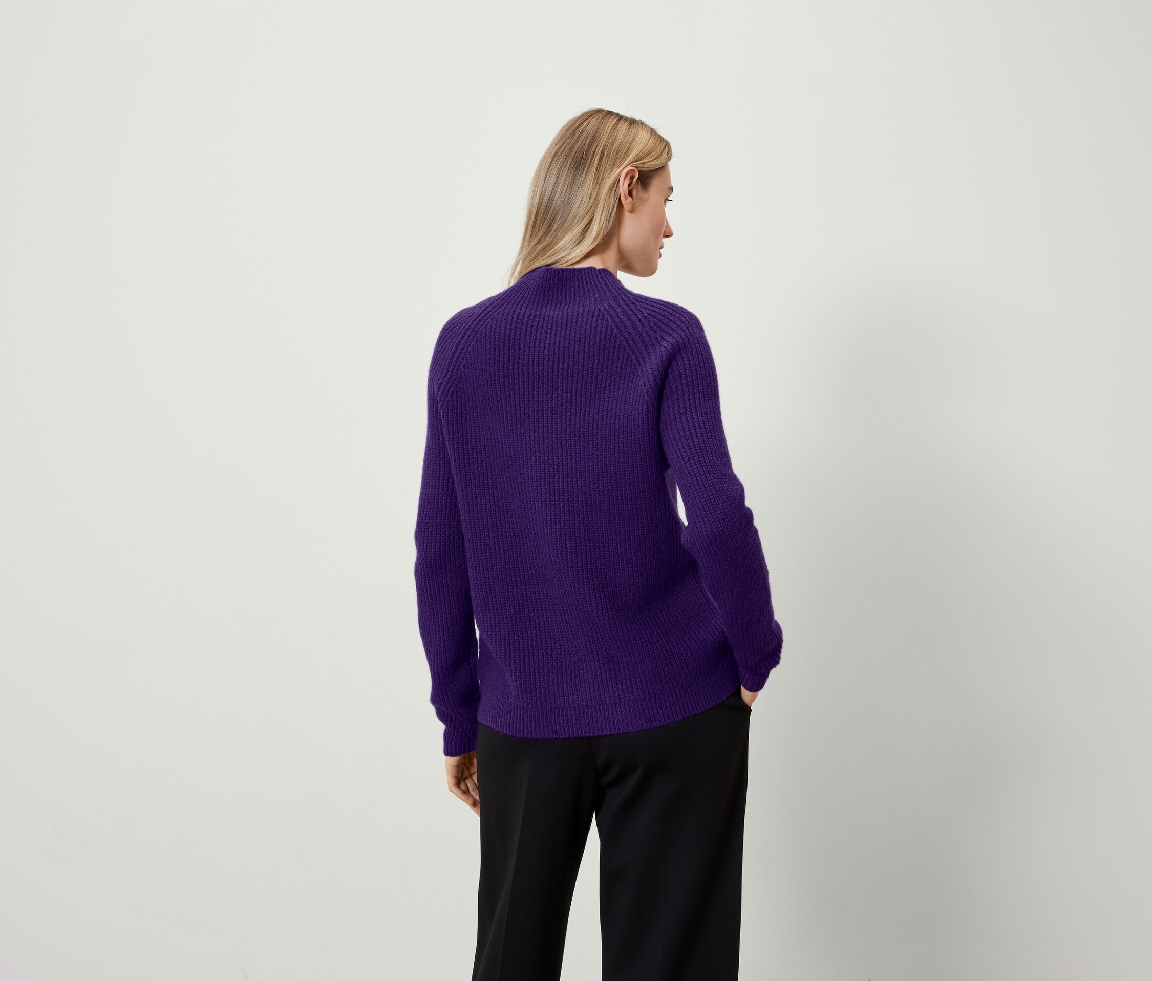 Sırtı kameraya dönük bir kadın, mor bir kazak ve siyah bir pantolon giyiyor.