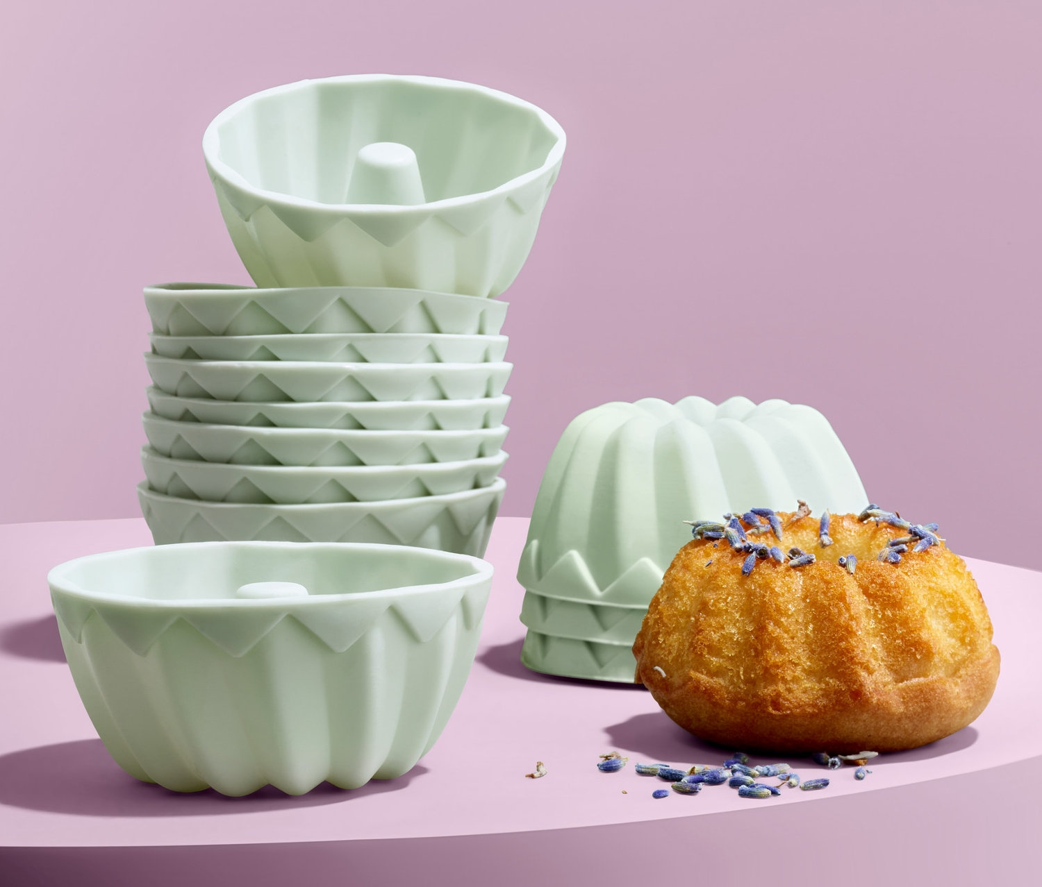 Mor bir arka plan üzerinde 12'li Mini Yuvarlak Kek Kalıbı, bir kekin üzeri lavanta ile kaplı.