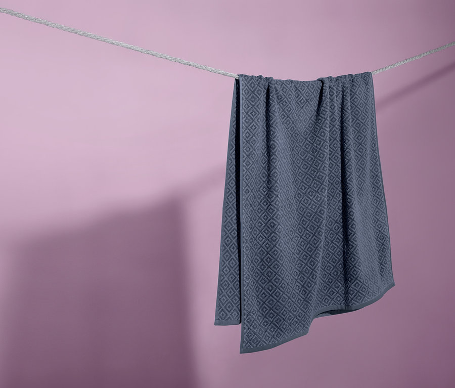Mor arka plan önünde çamaşır ipinde asılı duran mavi jakarlı banyo havlusu.