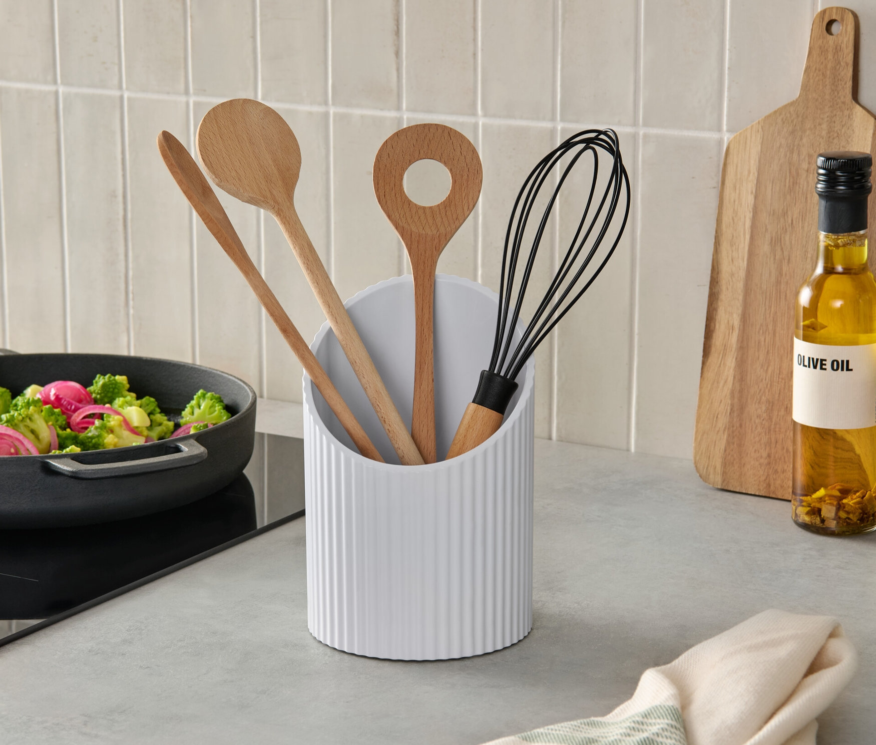 Ocakta sebze tavası ve yanında ahşap kaşıklar ve çırpma teli içeren bir malzeme standı olan mutfak sahnesi.