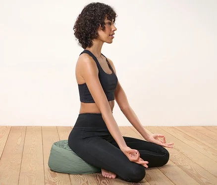 Kadın meditasyon minderi üzerinde oturmuş, mudra yapıyor.