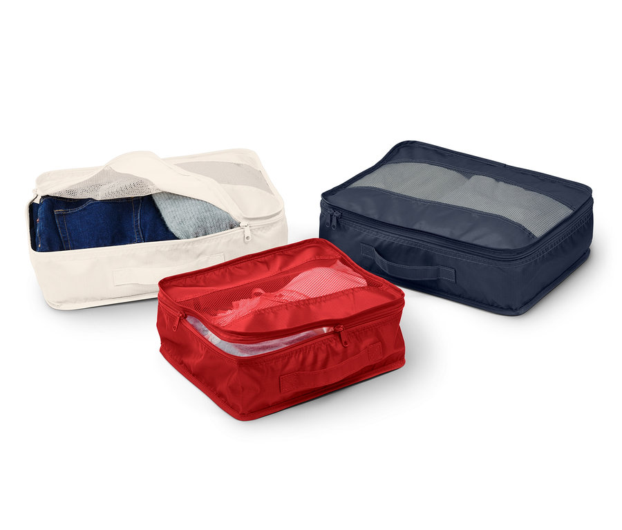 Üç adet bavul düzenleyici: biri içinde kot pantolon olan krem rengi, biri içinde giysi olan kırmızı ve biri içinde gri giysiler olan lacivert.