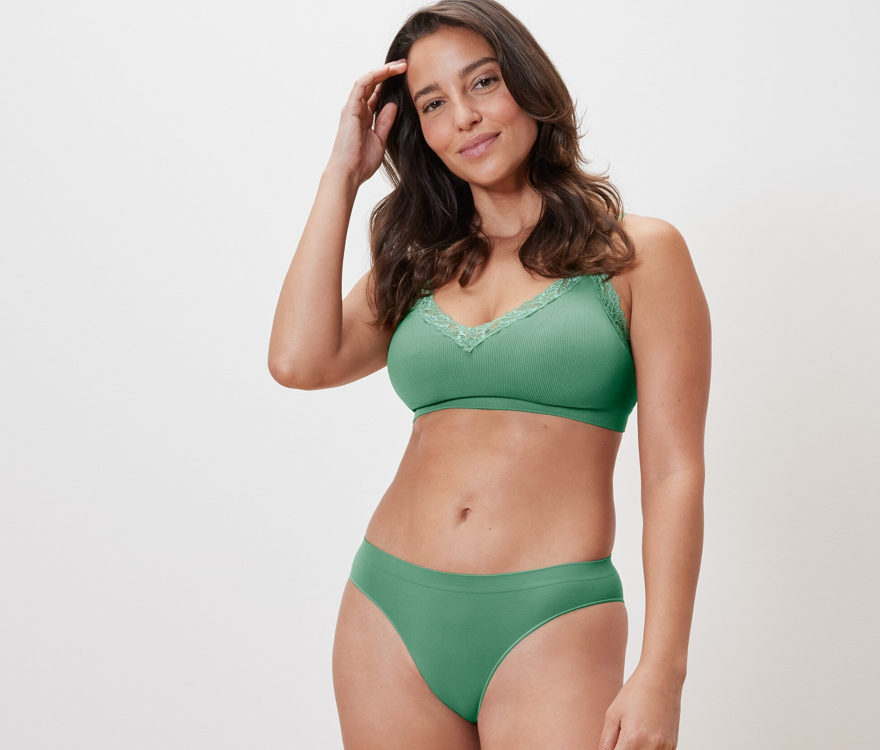 Kadın yeşil iç çamaşırıyla poz veriyor. Yeşil bir sütyen ve 2 adet yeşil dikişsiz slip külottan birini giyiyor.