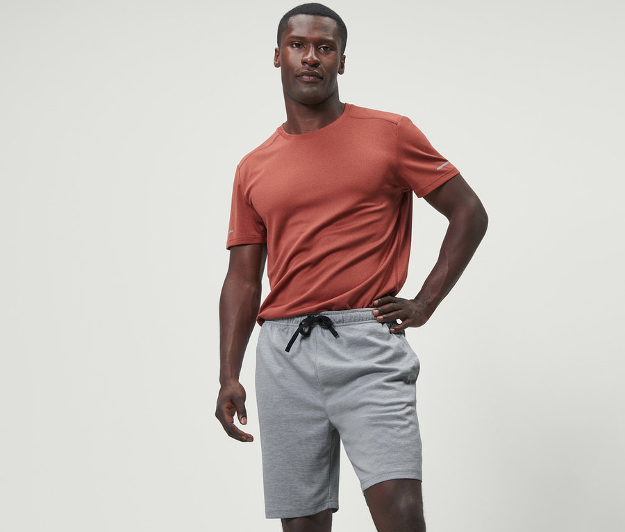 Adam gri spor şortu ve turuncu tişörtle poz veriyor.