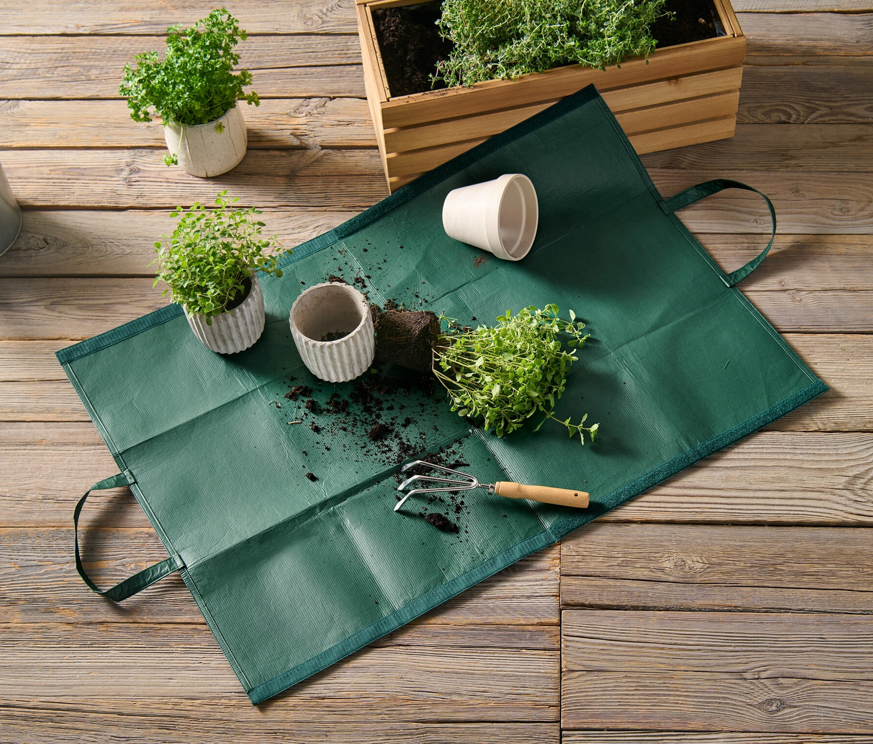 Bir bahçe atıkları çantası, saksı bitkileri ve bir sulama kabının yanında ahşap bir zeminde duruyor.