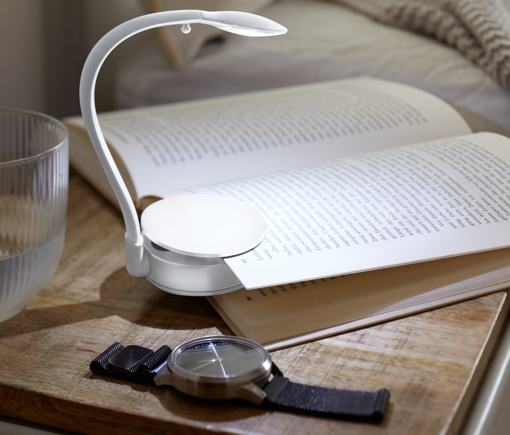 Açık bir kitap, bir komodinin üzerinde duruyor ve bir LED Okuma Lambası ile aydınlatılıyor.