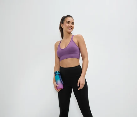 Spor sutyeni ve taytı giyen bir kadın su şişesi tutuyor.