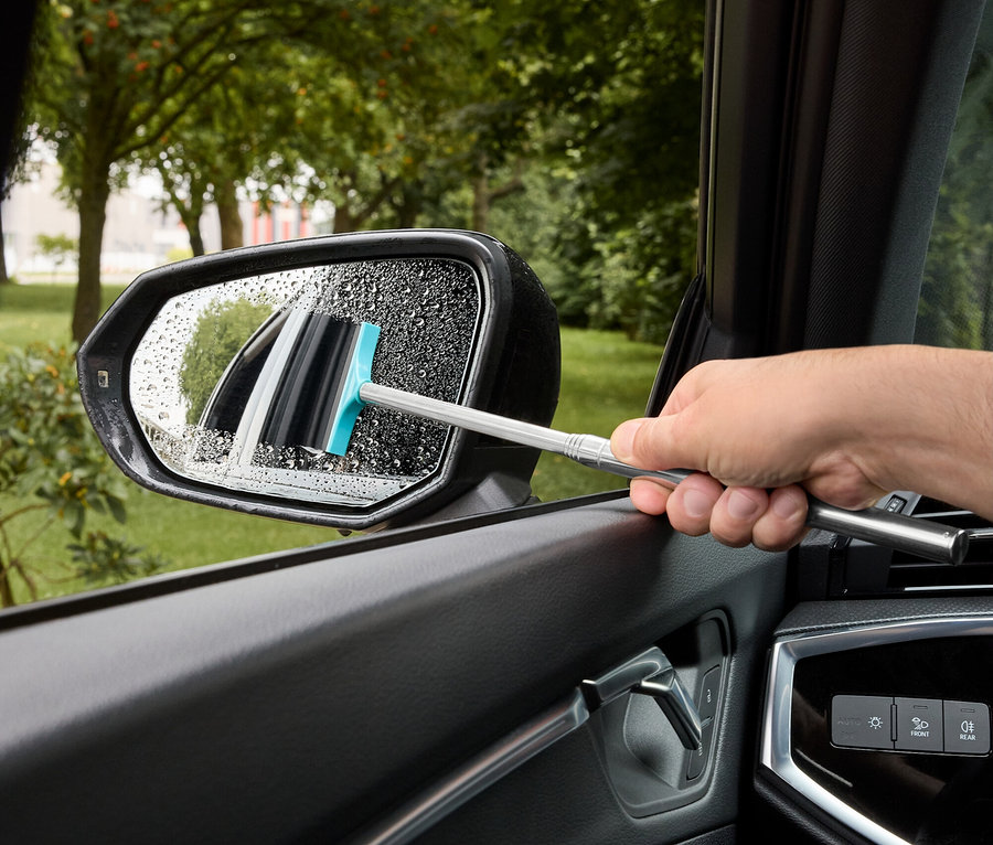 Adam, mavi lastikli bir silecek ile bir araba yan aynasından suyu siliyor.