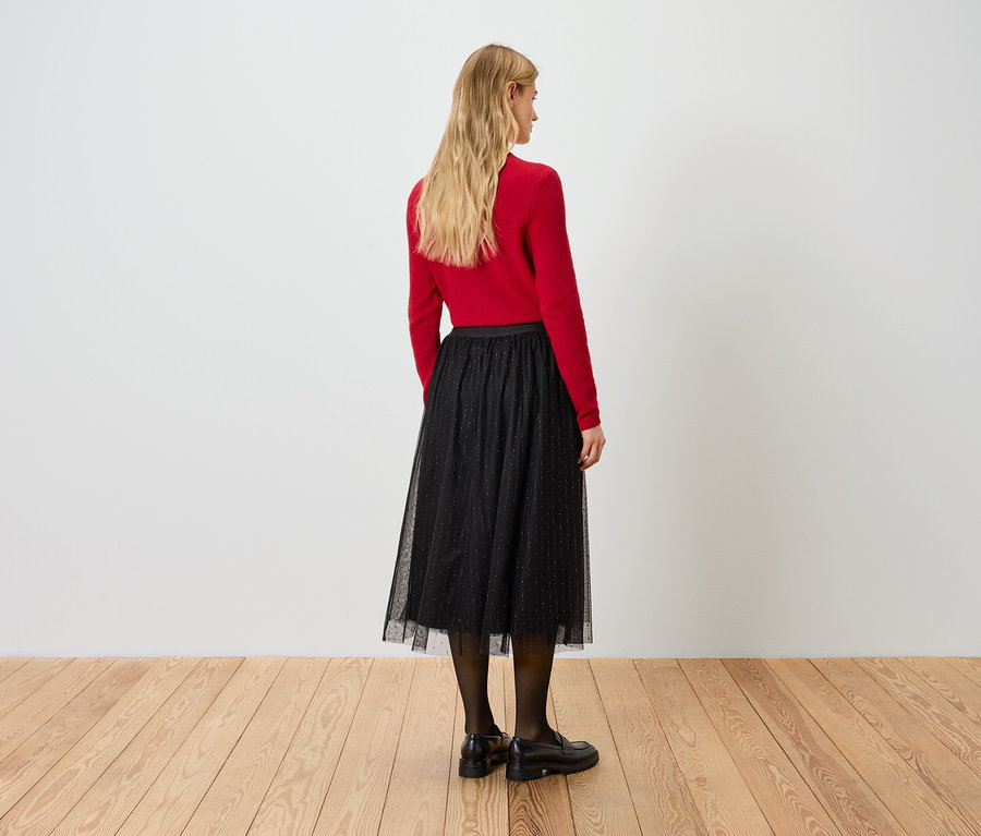 Sırtı kameraya dönük bir kadın kırmızı bir kazak ve siyah bir etek giyiyor.