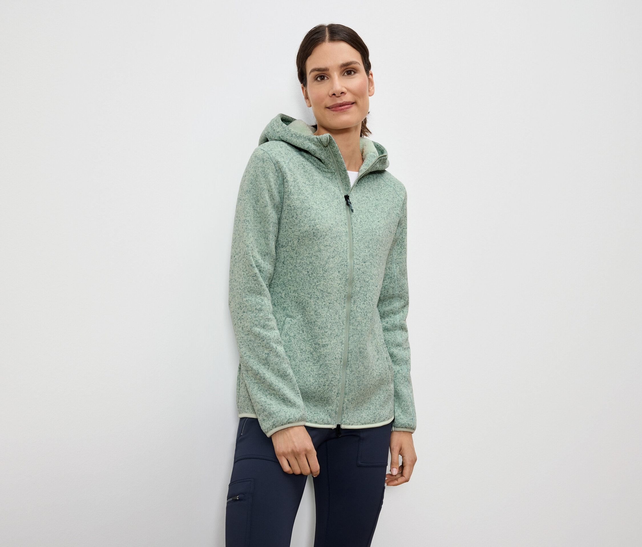 Kadın açık yeşil kapüşonlu fermuarlı polar ceket ve lacivert pantolon giyiyor.