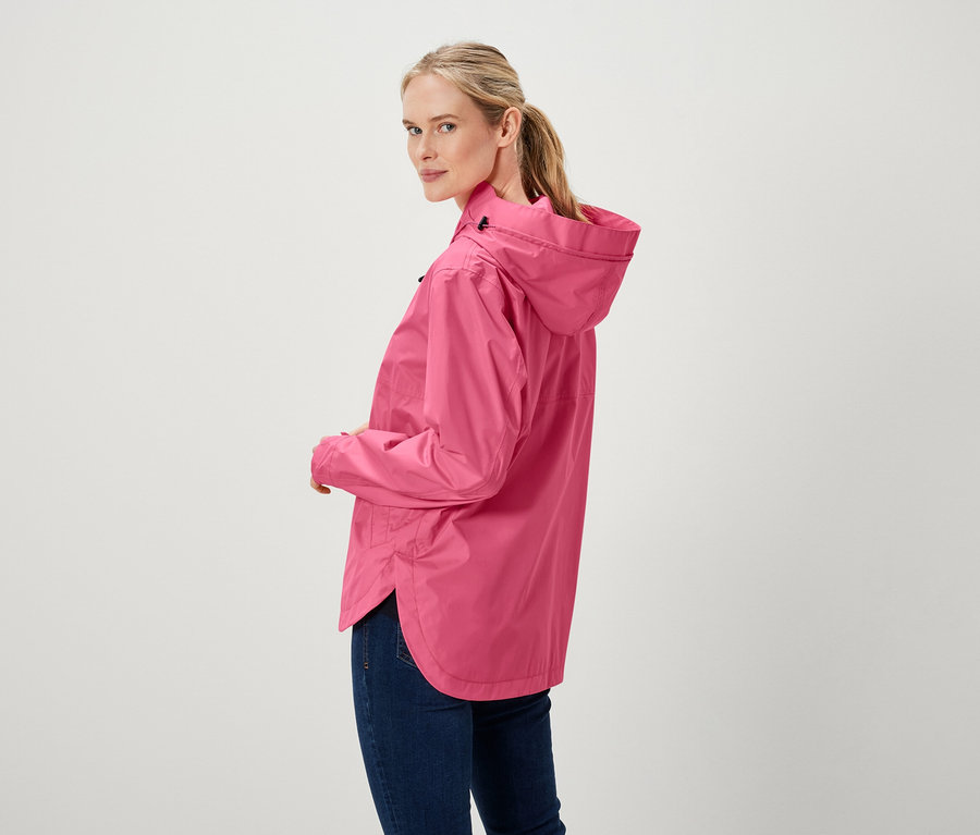 Kadın omzunun üzerinden bakıyor, pembe bir ceket ve kot pantolon giyiyor.