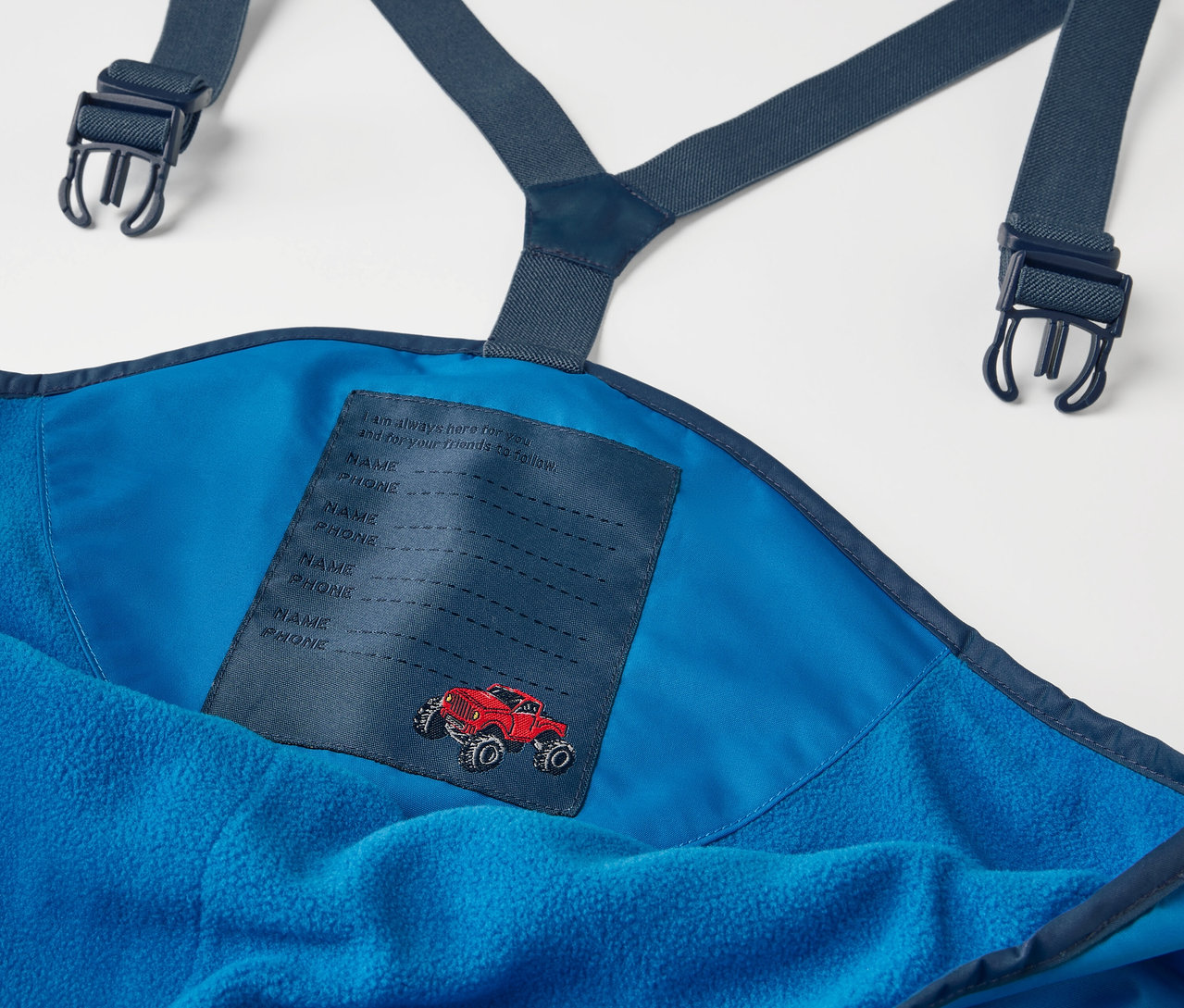 Askılı ve kırmızı araba yamalı, mavi çocuk termo yağmur pantolonunun yakın çekimi.