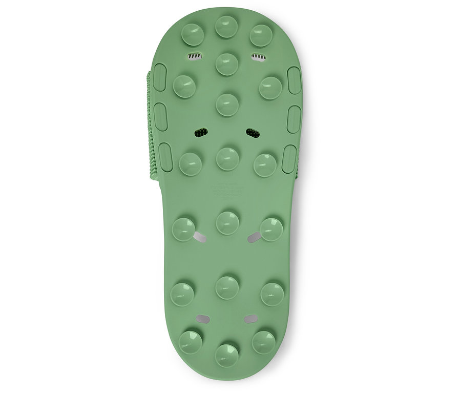 Beyaz bir arka plan üzerinde çıkıntıları olan tek bir yeşil banyo terliğinin yakın çekimi.