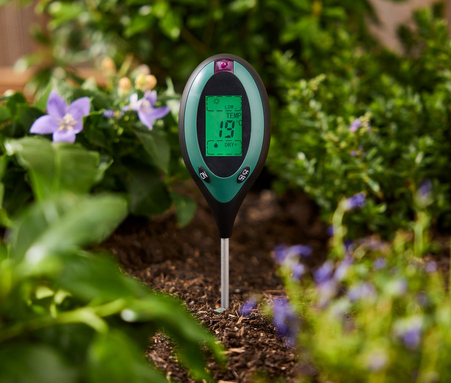 Yeşil bir toprak test cihazı, bitkilerin arasındaki toprağa saplanmış.