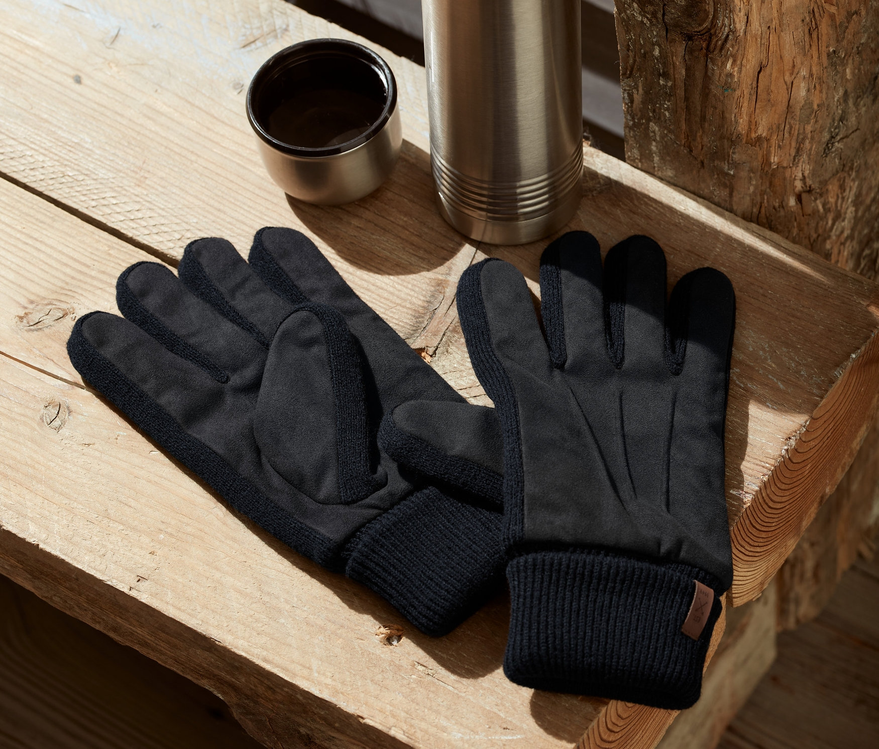 Ahşap bir bankta eldivenler, bir termos ve açık bir bardak duruyor.