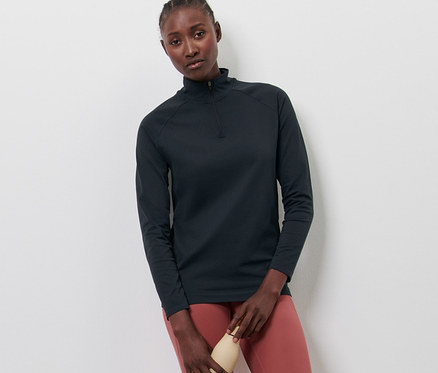 Kadın Seamless Antrenman Üstü, somon rengi tayt ve beyaz ayakkabılarla poz veriyor, elinde su şişesi var.