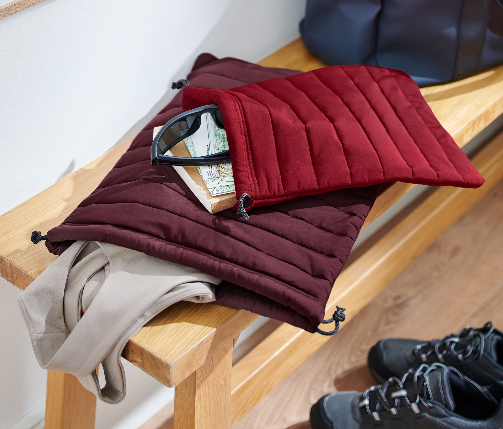 Bir bankta biri bordo diğeri vişne rengi olmak üzere 2 adet kapitone düzenleyici bulunmaktadır, içlerinde eşyalar vardır. Yerde ayakkabılar durmaktadır.