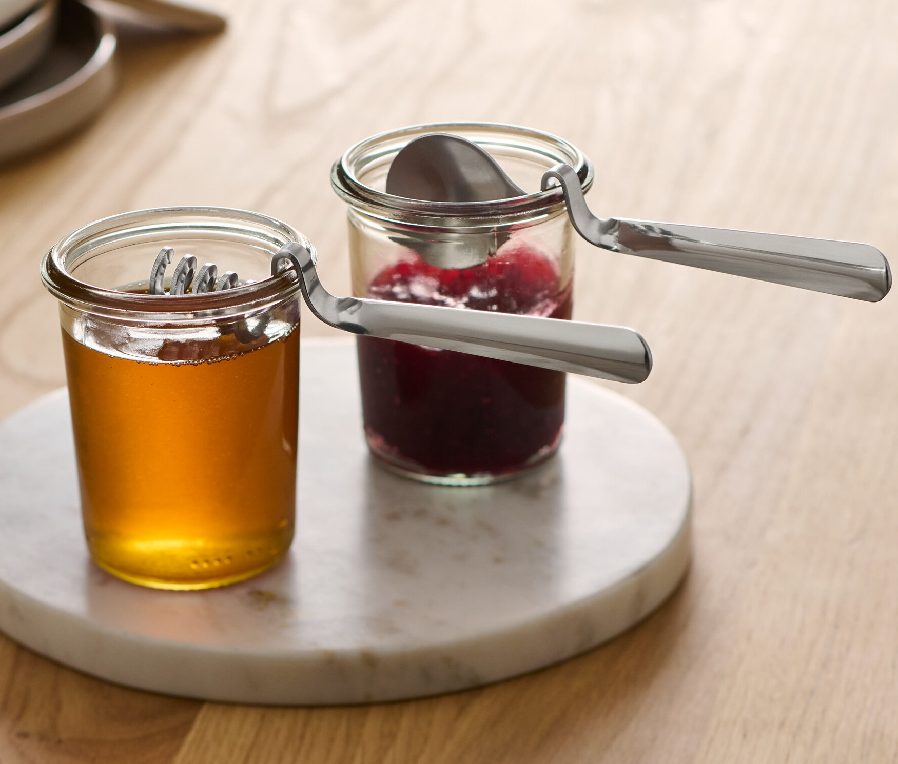 İki kavanoz bal ve reçel mermer bir tepside duruyor, her kavanozda bir Marmelat ve Bal Kaşığı var.